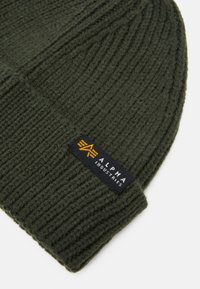 Zöld, bordázott kötött sapka, sárga és fekete "ALPHA INDUSTRIES" feliratozással az elkanyarodó peremen. Puha tapintású, testhezálló kialakítás.