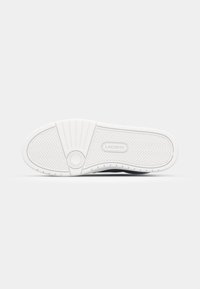 Lacoste-Schuhsohle, strukturierter weißer Gummi mit Fischgrätenmuster, kreisförmiger Akzent in der Mitte, mit geprägtem Logo an der Ferse.