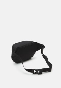 Melna jostas soma ar mīkstu dizainu, regulējamu siksnu un izturīgu plastmasas sprādzi. Gluda tekstūra ar vienkāršu, minimālistisku formu.