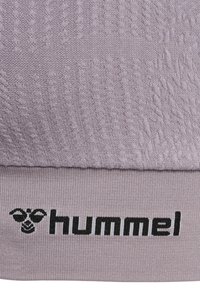 Lilla strikket stof med sort "hummel"-logo og stiliseret humle-design på nederste kant af tøjet.