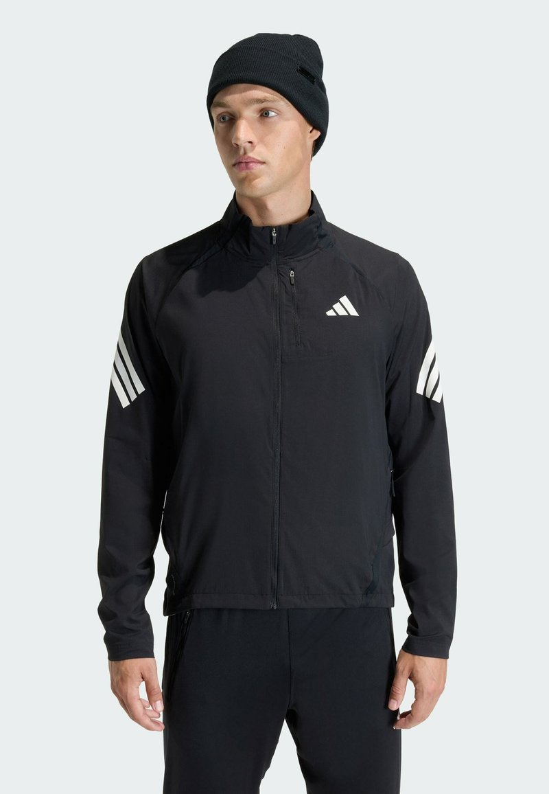 Black lightweight zip jacket with white Adidas logo and three-striped accents on shoulders, paired with a black knit beanie.