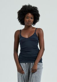 Canotta aderente di colore blu navy con spalline sottili e scollatura a V, abbinata a pantaloni da pigiama grigi di vestibilità ampia, con una texture del tessuto liscia.