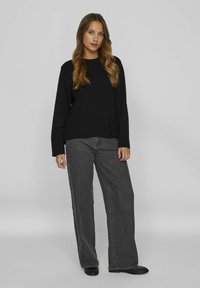 Pull en tricot noir avec un col rond, porté sur un jean en denim gris à jambes larges. Des chaussures noires plates viennent compléter la tenue, créant un look monochromatique.