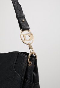 Černá kožená kabelka s texturovaným povrchem, zdobená zlatým kruhovým kováním a odnímatelným popruhem.
