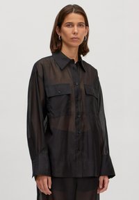 Zwarte sheer blouse met lange mouwen, knoopsluiting aan de voorkant, twee borstzakken en een klassieke kraag. Glad textuur en lichtgewicht stof.