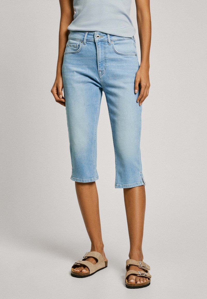 Heledad sinised denim capri püksid keskmise tõusuga, nupulukuga, ettepoole taskud ja keeratud servad. Koos beeži sandaalidega.