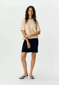 Beige knit sweater with short sleeves, paired with a black mini skirt featuring a side slit. Model wearing black flip-flops.