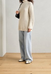 Beige geribbelde coltrui gecombineerd met lichtblauwe wijde jeans en witte schoenen met zwarte accenten. Eenvoudige zwarte handtas inbegrepen.