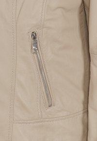 Beige läderjacka med struktur, som har en dragkedjeficka på vänster sida och kontrasterande sömdetaljer.