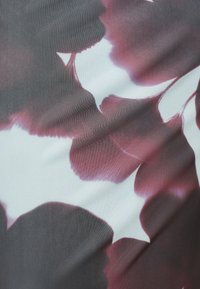 Κοντινό πλάνο υφάσματος με μεγάλο αφηρημένο φλοράλ σχέδιο σε σκούρες κόκκινες και λευκές αποχρώσεις, που δείχνει την υφή και ελαφριές πτυχώσεις.