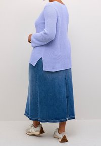 Pull en tricot violet clair avec des manches longues, associé à une jupe maxi en denim. La tenue présente des fentes sur les côtés et des baskets blanches.