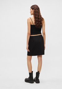 Zwart nauwsluitend hemdje en zwarte knie-lange rok met een gladde afwerking, gecombineerd met zwarte enkellaarsjes met een chunky zool.