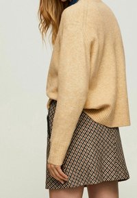 Maglione beige chiaro con orlo a costine, abbinato a una mini gonna a fantasia con design a pied de poule marrone e nero e dettaglio con zip.