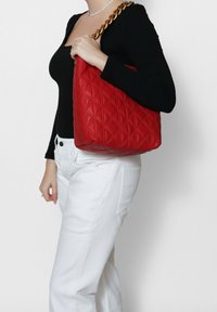 Borsa a tracolla rossa trapuntata con una forma strutturata, dotata di una tracolla in catena dorata. La texture della borsa è liscia, accentuata da un motivo a diamante.