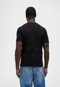 Μαύρο κοντομάνικο t-shirt, με στρογγυλή λαιμόκοψη, κατασκευασμένο από μαλακό ύφασμα; σε συνδυασμό με ανοιχτό μπλε τζιν, που αναδεικνύει μια χαλαρή εφαρμογή και υφή από τζιν.