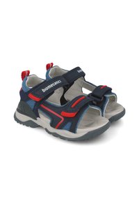 Sandalias azules y grises con acentos rojos. Fabricadas de textil y goma, cuentan con tiras ajustables de Velcro y una suela texturizada para mayor tracción.