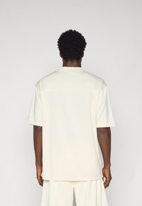 Cremefarvet polo-shirt med korte ærmer, glat tekstur og en subtil sømdetalje på tværs af ryggen, parret med matchende bukser.