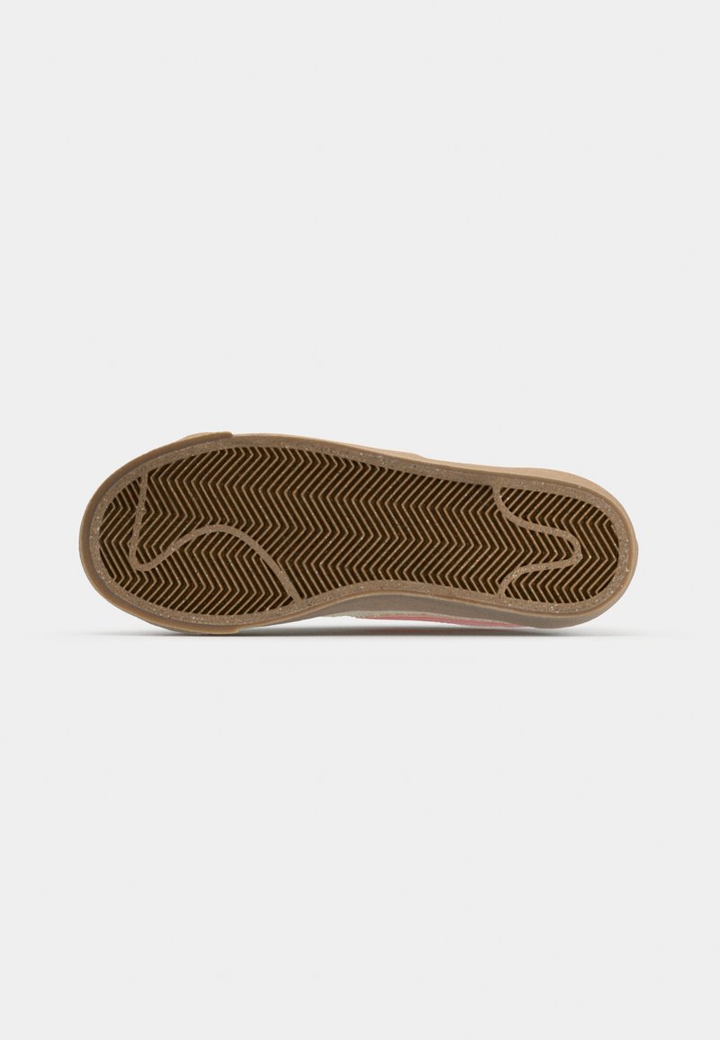 Semelle de chaussure de sport avec motif en chevrons, en caoutchouc beige, forme contournée et détail de branding subtil près du talon.