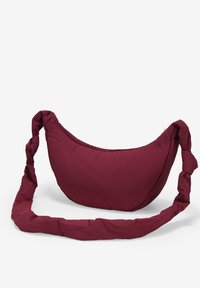 Borsa a spalla in tessuto bordeaux con forma arrotondata, texture simile a un cuscino e una tracolla attorcigliata per il trasporto. Presenta una chiusura con zip.