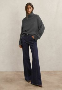 Grijze gebreide coltrui met geribbelde manchetten, gecombineerd met donkerblauwe uitlopende jeans met lichte stiksels en een gladde textuur.