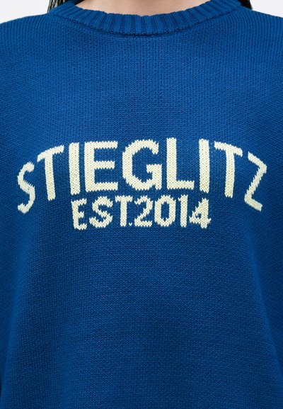 Plavi pleteni pulover s bijelim tekstom na kojem piše "STIEGLITZ" i "EST. 2014." Riblji izrez i mekana tekstura.