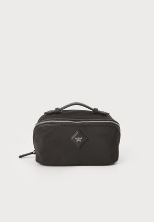 Trousse de toilette noire en nylon avec une poignée supérieure, fermeture éclair et accent de logo en diamant. Elle présente une texture lisse et une forme rectangulaire compacte.
