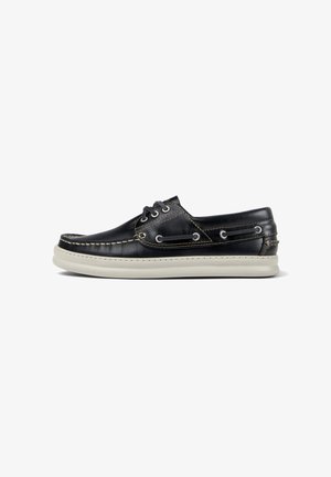 Schwarza lederschuh mit weißer gummisohle, verziert mit dekorativen nähten und metallösen für die schnürsenkel. Klassisches design mit minimalen akzenten.