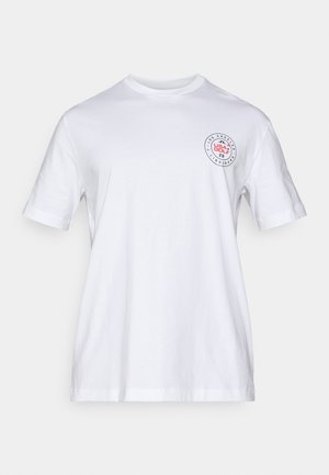 White cotton t-shirt with a round neckline and short sleeves. Features a printed circular logo in red and black on the left chest area.
