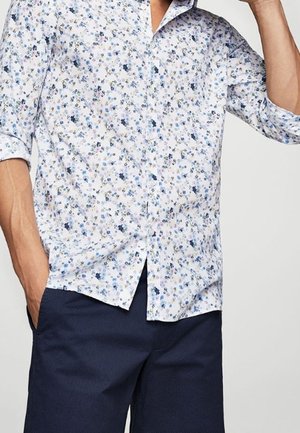 Camicia bianca con motivo floreale blu, design con bottoni, maniche lunghe arrotolate, abbinata a pantaloni corti blu scuro. Materiale in cotone, vestibilità casual.