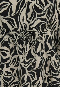 Tissu de robe noir et beige présentant un motif abstrait audacieux avec des contours sombres. Comprend un détail de taille cintrée avec des liens réglables.