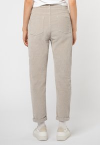 Lichtbeige corduroybroeken met een rechte pijp, opgerolde mouwen, twee achterzakken en een gestructureerd oppervlak. Ggedragen met witte sneakers.