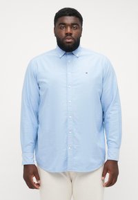 Camicia button-up azzurro chiaro con maniche lunghe, colletto classico, bottoni bianchi e un piccolo emblema sul petto sinistro.
