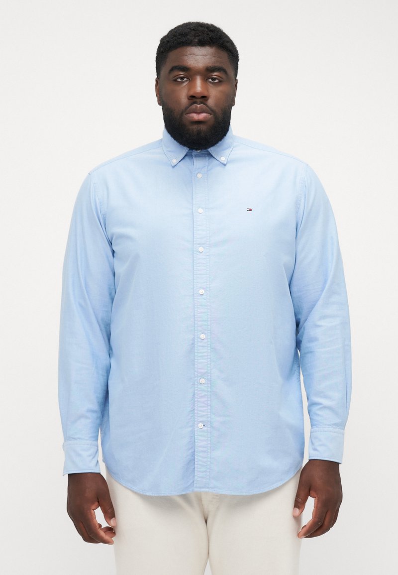 Camicia button-up azzurro chiaro con maniche lunghe, colletto classico, bottoni bianchi e un piccolo emblema sul petto sinistro.