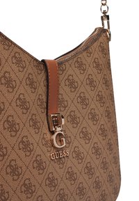 Sac à main brun à motifs fabriqué en matériau texturé, avec une bandoulière en cuir et un accent en métal avec le logo Guess. Fermeture éclair lisse sur le dessus.