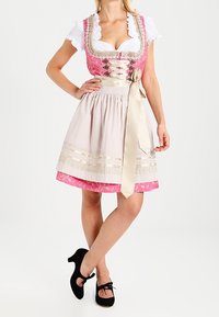 Robe traditionnelle dirndl avec corsage rose à lacets, chemisier blanc, jupe à carreaux et ruban crème. Chaussures noires complètent la tenue.