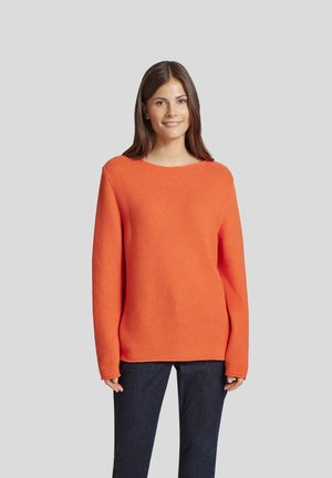 Oranges Strickpullover mit weitem Ausschnitt und langen Ärmeln, mit einer strukturierten Oberfläche. Kombiniert mit dunklen Jeans für einen Kontrast.