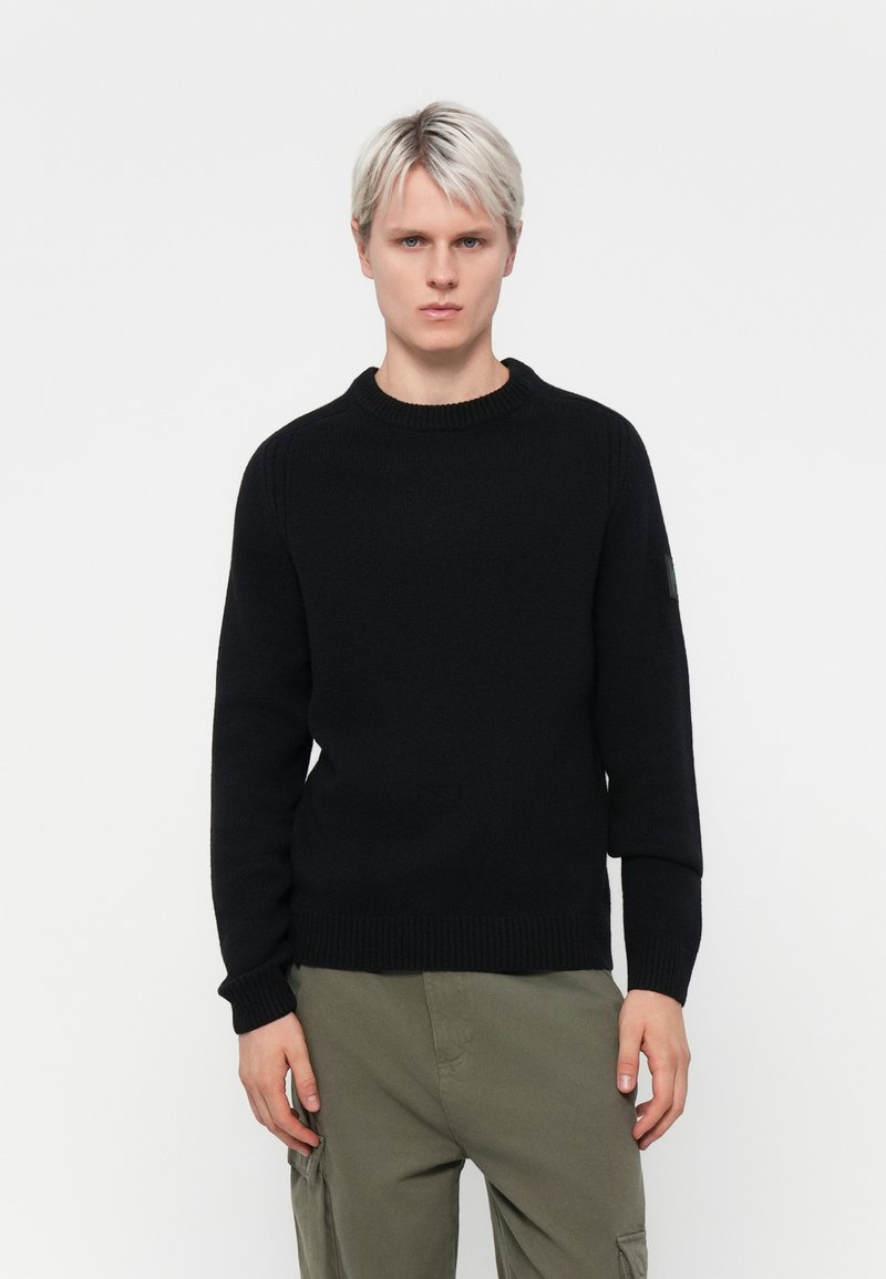Pulover negru tricotat cu guler și manșete cu bandă. Design simplu, țesătură texturată. Asortat cu pantaloni cargo de culoare măslinie deschisă.