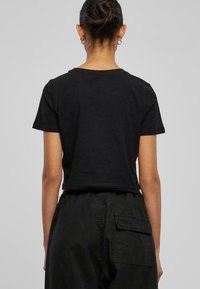 Tricou negru scurt cu mâneci scurte, fabricat din bumbac moale. Hainele au o tăietură dreaptă la spate; textură netedă fără modele vizibile sau accesorii.