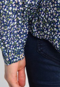 Langärmlige, knopf-пlicant Bluse in Marineblau mit floralem Muster in Pink und Grün, aus leichtem Stoff mit leicht strukturiertem Oberflächen.