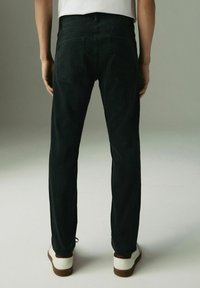 Zwarte denim jeans met een rechte pijp, twee achterzakken en een gladde textuur. Gedragen met witte sneakers met bruine accenten.