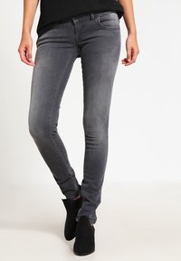 Jeans ajustados grises de mezclilla, con un lavado medio, diseño de cinco bolsillos y detalles de desvanecimiento sutil. Combinados con botas negras hasta el tobillo.