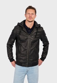 Sort læderjakke med grå hætte, lynlås lukning, sidelommer, ribbede manchetter og kant. Bæres over en mørk polo skjorte med tydelig søm.