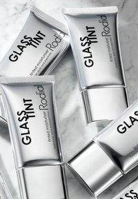 Vier silberne Tuben mit Tönungsmousse, gekennzeichnet mit "Glass Tint" und "Rodial" auf einem hellen Marmelhintergrund, die schlanke, moderne Designs zeigen.