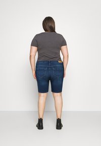 Sötétkék farmer rövidnadrág közepes derékkal, két hátsó zseb finom designnal, egy testhezálló szürke pólóval és fekete bokacsizmával párosítva.