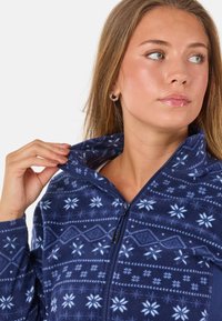 Granatowy polar na zamek z wzorami śnieżynek i geometrycznymi. Posiada wysoki kołnierz i gładką teksturę, z dopasowanym krojem.