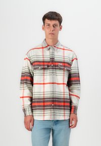 Camisa de franela en un patrón de cuadros en blanco, gris y rojo, con cierre frontal de botones, dos bolsillos en el pecho y mangas largas. Textura de tela suave.