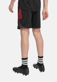 Svarta idrottsshorts med röda accentsträck, svarta fotbollsskor och svarta strumpor med vita horisontella ränder, sedd bakifrån.