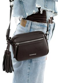 Hnědá kožená crossbody taška s zipovým uzávěrem, texturovaným povrchem a dekorativním třásním. Název značky "EMILY&NOAH" je umístěn na přední straně.