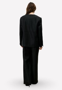 Zwarte op maat gemaakte blazer en bijpassende wijde pantalon. Beide kledingstukken hebben een gladde textuur en een minimalistisch ontwerp met strakke lijnen.