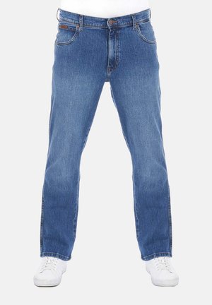 Jeans in denim azzurro chiaro con taglio dritto, cinque tasche, dettagli cuciti e chiusura con bottone. Indossati con sneaker bianche.